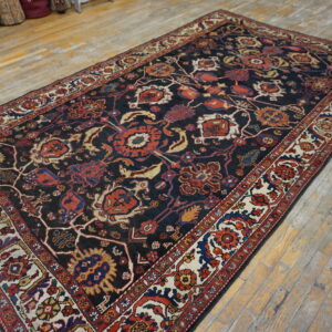 Navy rug with dense red and cream traditional floral patterns lies on light, rustic hardwood planks.