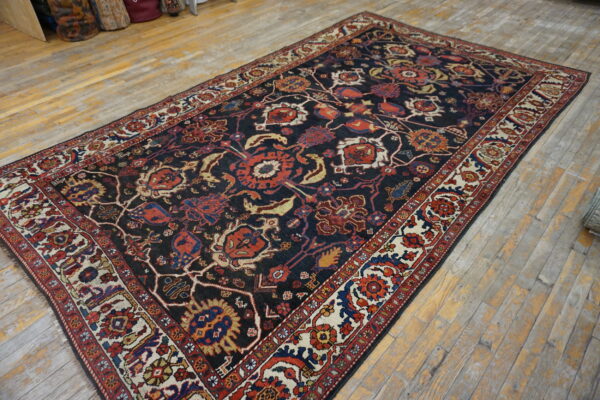 Navy rug with dense red and cream traditional floral patterns lies on light, rustic hardwood planks.
