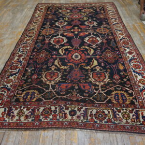 Dark blue rug with complex red, gold, and cream traditional motifs displayed on distressed wood flooring.