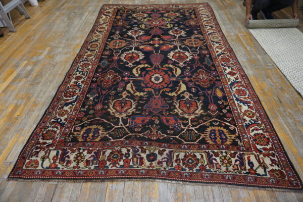 Dark blue rug with complex red, gold, and cream traditional motifs displayed on distressed wood flooring.