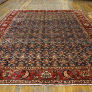 Large blue and red rug with an all-over repeating paisley pattern laid on wide wood floorboards.