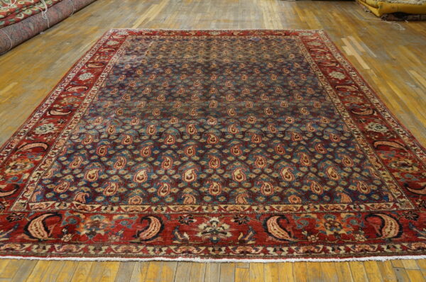 Large blue and red rug with an all-over repeating paisley pattern laid on wide wood floorboards.