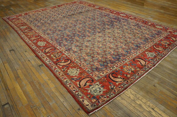 Low pile rug featuring a faded blue paisley field and contrasting wide red border on worn wood planks.