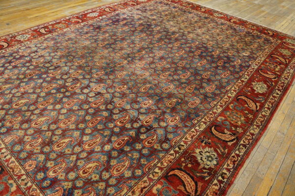 Traditional blue and red rug featuring an intricate field of paisley motifs on pale wood planks.