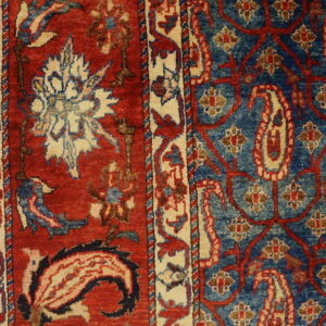 Red and blue rug detail showing floral borders meeting a field of paisley and scrolling vines on wood flooring.