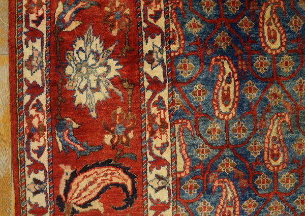 Red and blue rug detail showing floral borders meeting a field of paisley and scrolling vines on wood flooring.