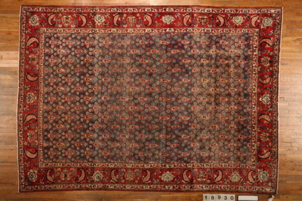 Low-pile rug with a repeating teal and red paisley pattern and wide decorative red borders on wood floors.