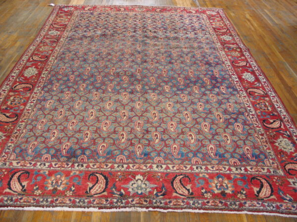 Blue rug with repeating cream paisley motifs and crimson floral borders covers a wood plank floor.