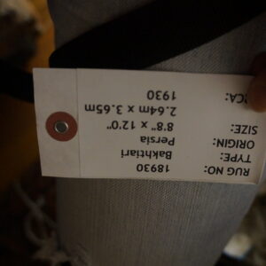 A hand holds a white identification tag against the textured surface of a tightly rolled light gray rug.