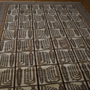 Geometric brown and cream rug with a tiled pattern featuring stylized vertical abstract designs on hardwood.