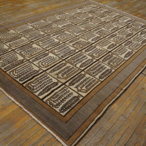Beige and brown low-pile rug featuring stylized motifs within a geometric grid pattern on wood flooring.