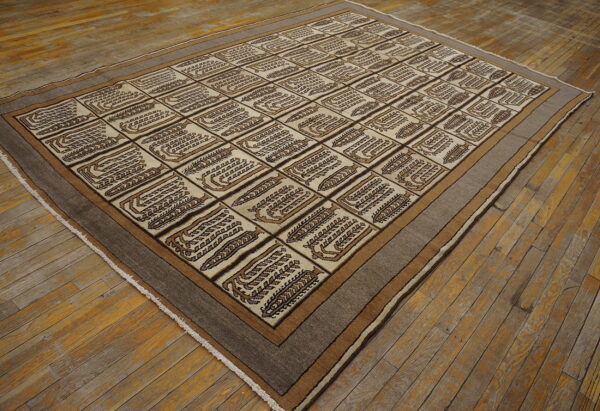 Beige and brown low-pile rug featuring stylized motifs within a geometric grid pattern on wood flooring.