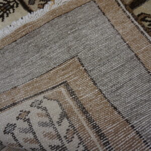 Folded rug displays its woven gray and brown striped backing next to a detailed beige and brown pile.