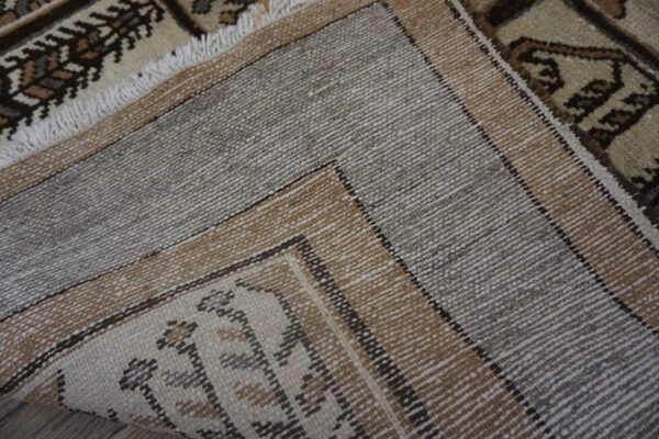Folded rug displays its woven gray and brown striped backing next to a detailed beige and brown pile.