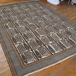 Beige and brown rug featuring a grid design of abstract trees, surrounded by a broad gray border on wood flooring.