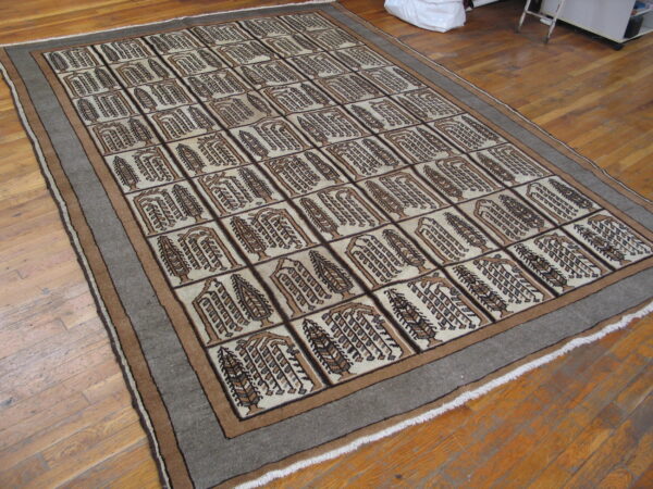 Beige and brown rug featuring a grid design of abstract trees, surrounded by a broad gray border on wood flooring.