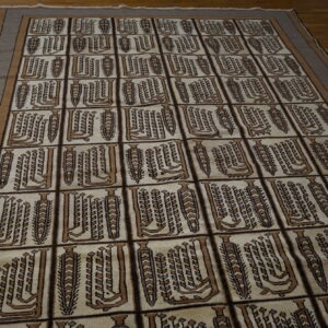 A cream rug with brown rectangular repeating geometric patterns and a striped border rests on a dark wood floor.