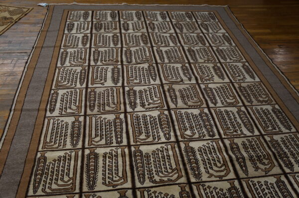 A cream rug with brown rectangular repeating geometric patterns and a striped border rests on a dark wood floor.