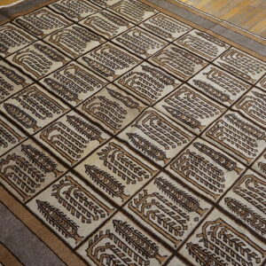 Beige rug featuring repeated brown and tan stylized tree motifs within a rectangular grid, placed on wood floors.