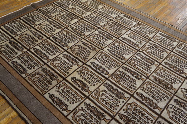 Beige rug featuring repeated brown and tan stylized tree motifs within a rectangular grid, placed on wood floors.