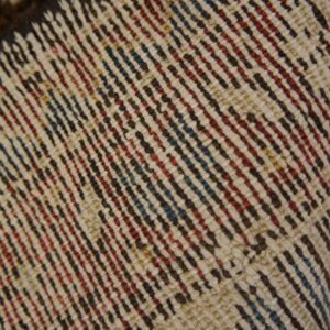 Diagonal pattern detail of a tightly woven rug in shades of cream, red, blue, and dark brown.