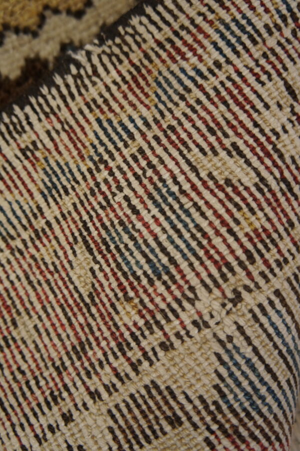 Diagonal pattern detail of a tightly woven rug in shades of cream, red, blue, and dark brown.