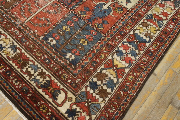 A compartmentalized rug featuring pictorial trees in red, blue, and brown squares rests on worn wood flooring.