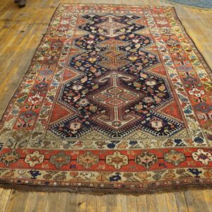 Long traditional rug in navy, red, and cream geometric patterns rests on worn wood flooring.