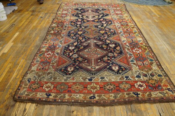 Long traditional rug in navy, red, and cream geometric patterns rests on worn wood flooring.