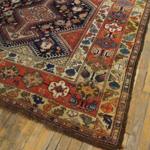 A patterned rug with rust red and navy colors rests on light, worn wooden plank flooring.