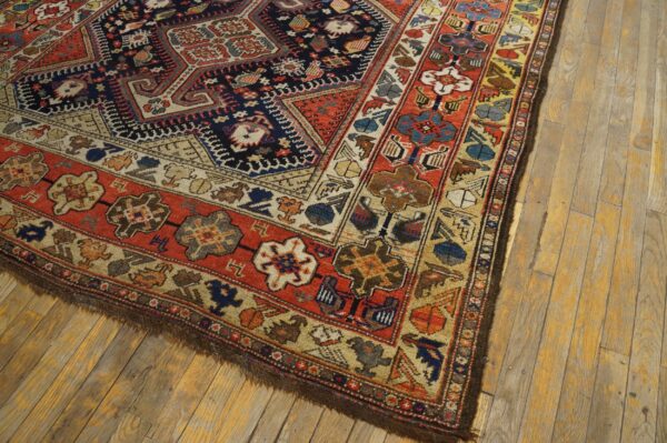 A patterned rug with rust red and navy colors rests on light, worn wooden plank flooring.