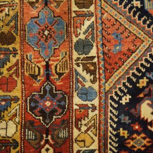 Detailed view of a geometric rug with red, blue, and gold patterns next to light colored wood flooring.