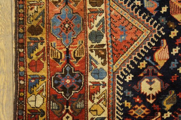 Detailed view of a geometric rug with red, blue, and gold patterns next to light colored wood flooring.