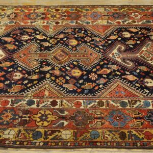 Dark blue rug with stylized avian and geometric patterns, framed by wide borders in red, cream, and yellow.