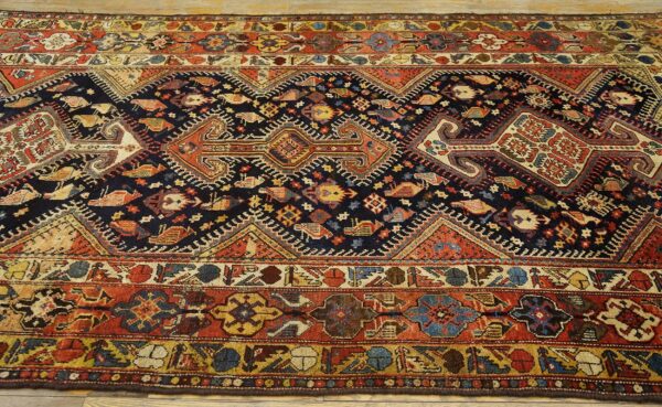 Dark blue rug with stylized avian and geometric patterns, framed by wide borders in red, cream, and yellow.