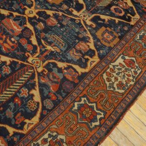 Dark blue rug with rust and gold geometric patterns lies diagonally across wide plank wood flooring.