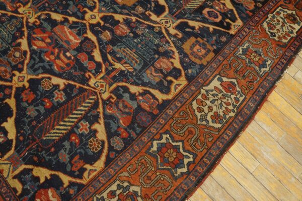 Dark blue rug with rust and gold geometric patterns lies diagonally across wide plank wood flooring.