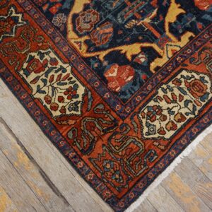Close-up of a complex navy and rust patterned rug corner with cream accents on faded wood floorboards.