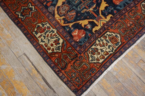 Close-up of a complex navy and rust patterned rug corner with cream accents on faded wood floorboards.