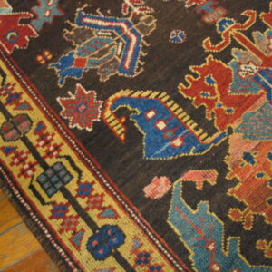 Low-pile rug with geometric blue, red, and gold designs on a dark field over wood planks.