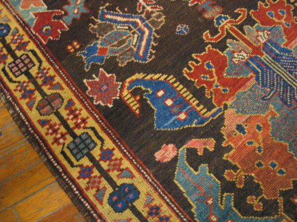 Low-pile rug with geometric blue, red, and gold designs on a dark field over wood planks.