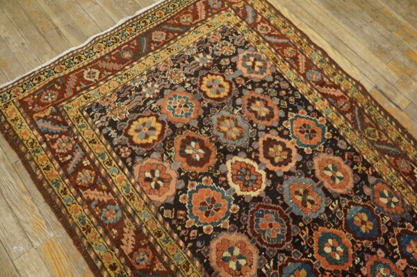 Ornate rug featuring orange, teal, and gold medallions on a black ground with wide rust borders on wood flooring.