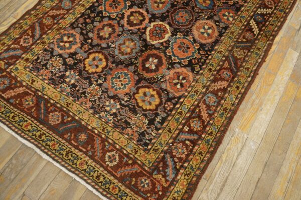 A detailed view of a dark floral patterned rug with rust and blue motifs placed on light wooden floors.