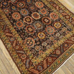 A dark patterned rug with rosette medallions and rust borders rests on distressed light wood floors.