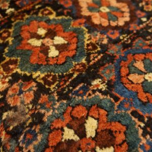 Close-up of a dense, textured rug pattern featuring red, teal, blue, and black stylized florals.