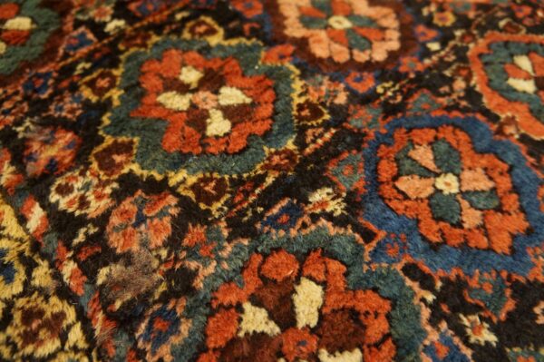 Close-up of a dense, textured rug pattern featuring red, teal, blue, and black stylized florals.