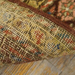 Close-up of a rug's tightly woven backing, dark brown edge binding, and multicolored low pile on wood flooring.