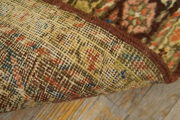 Close-up of a rug's tightly woven backing, dark brown edge binding, and multicolored low pile on wood flooring.