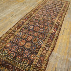 Low-pile dark runner with blue, rust, and pink repeating medallions on distressed wood flooring.