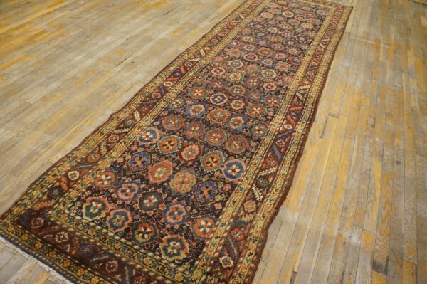 Low-pile dark runner with blue, rust, and pink repeating medallions on distressed wood flooring.